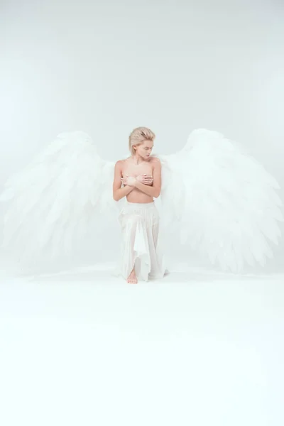 白い背景にポーズをしながら乳をカバー天使の翼を持つ美しい若い女性 — ストック写真