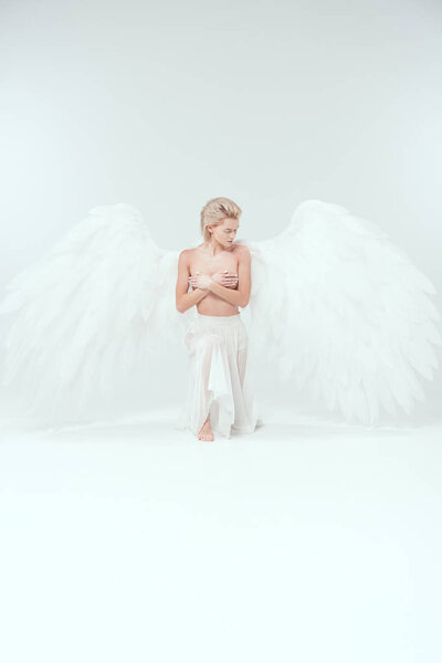beautiful young woman with angel wings covering breasts while posing on white background