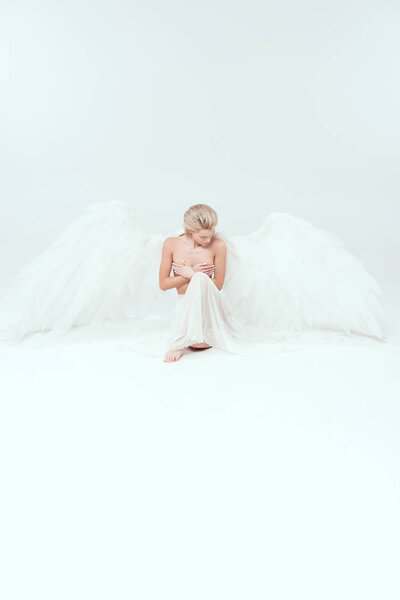 beautiful woman with angel wings sitting and posing isolated on white with copy space