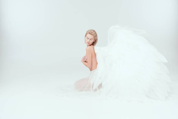 Beautiful woman with angel wings sitting and posing isolated on white with copy space