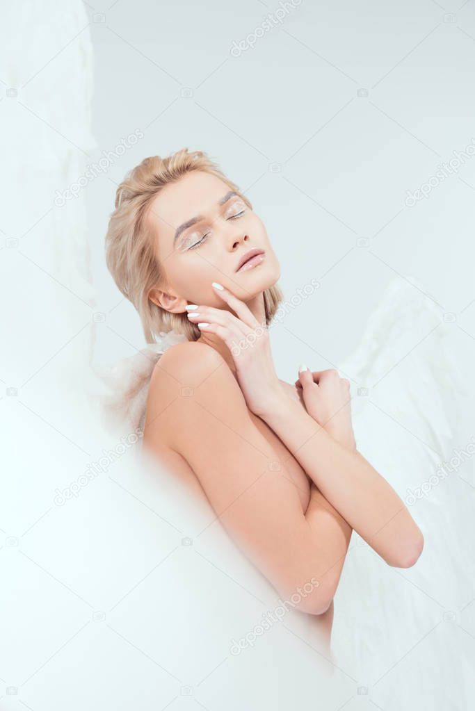 selective focus of beautiful woman with angel wings posing with eyes closed isolated on white