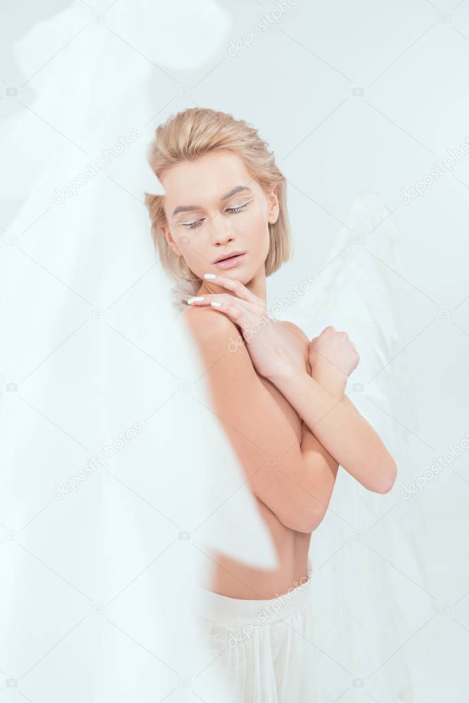 selective focus of beautiful woman with angel wings posing with eyes closed isolated on white