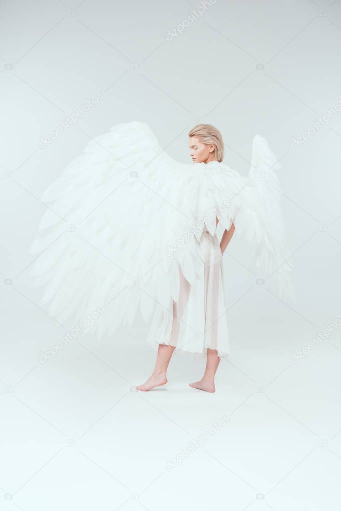 beautiful young woman with angel wings looking away and posing isolated on white