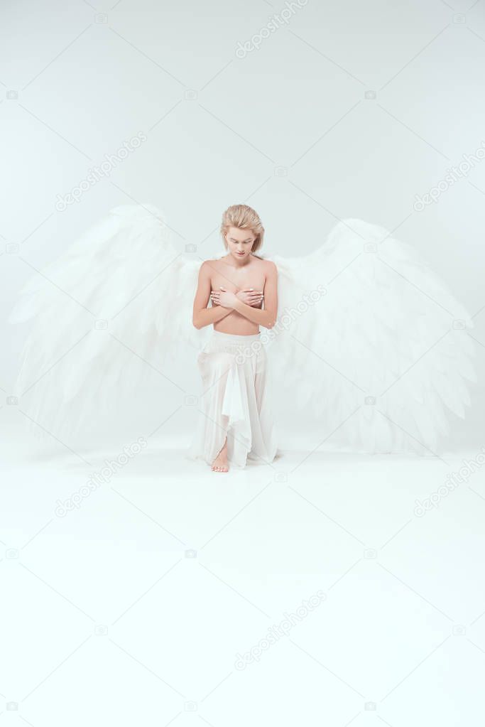beautiful tender woman with angel wings covering breasts while posing isolated on white
