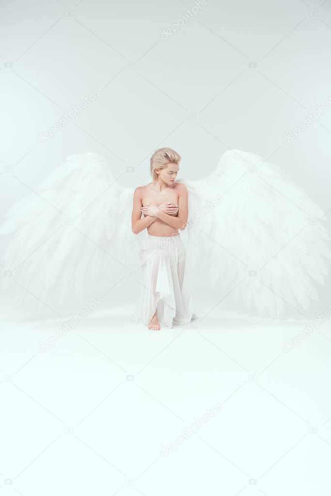 beautiful young woman with angel wings covering breasts while posing on white background
