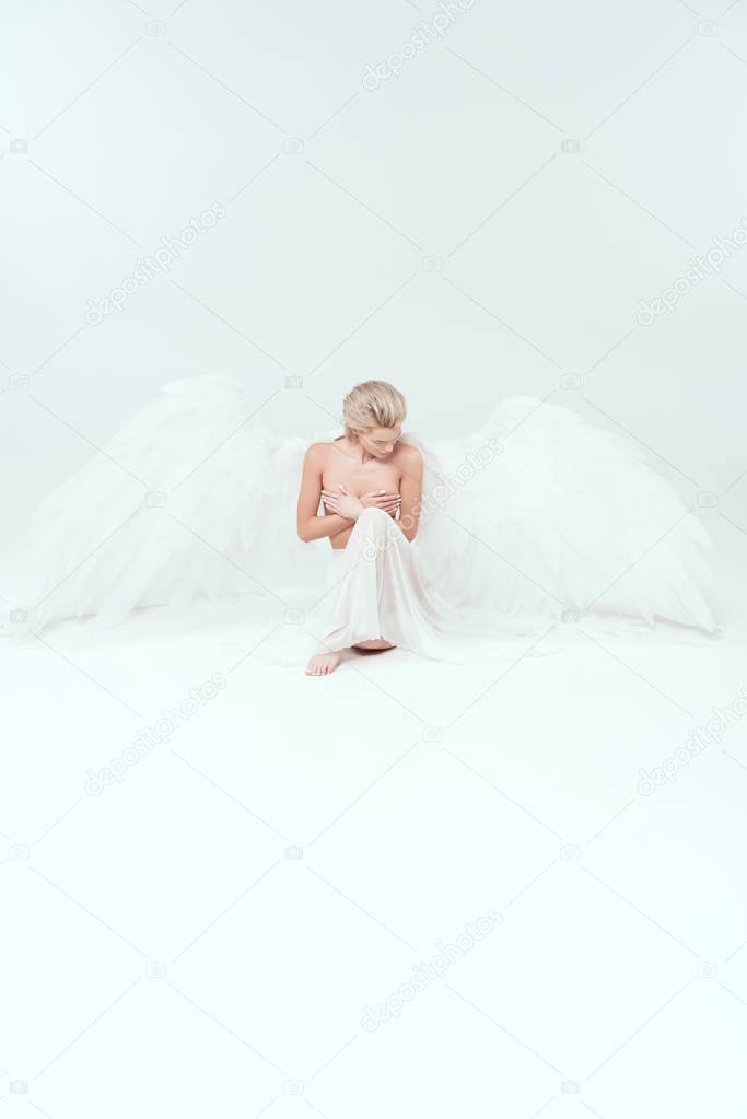 beautiful woman with angel wings sitting and posing isolated on white with copy space