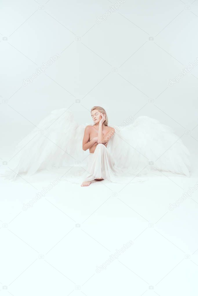 beautiful woman with angel wings covering breasts and posing isolated on white with copy space