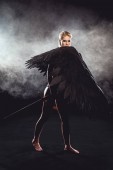 beautiful woman with angel wings holding sword and posing on black background
