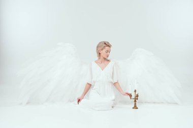 beautiful woman in angel costume with wings sitting near candelabrum with candles isolated on white clipart