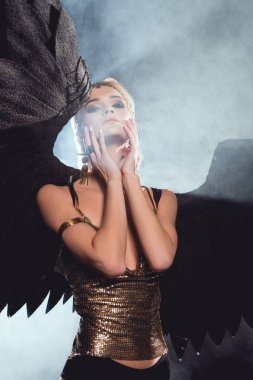 kara melek kanatları ve yüz dokunmaktan ve dumanlı arka plan üzerinde poz altın aksesuarları ile güzel seksi kadın