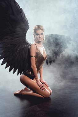 güzel seksi kadın oturuyor, koyu arka plan üzerinde poz ve kameraya bakarak kara melek kanatlı