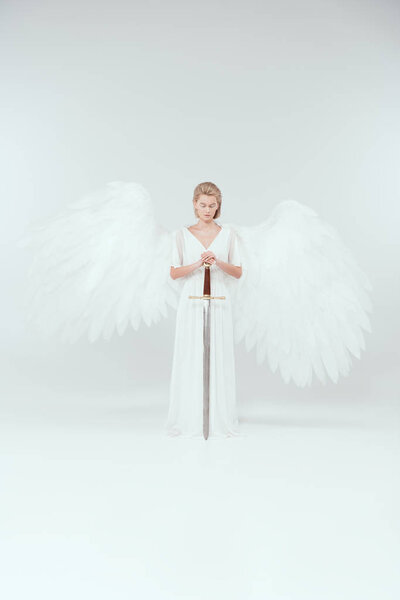 beautiful woman with angel wings holding sword and posing on white background