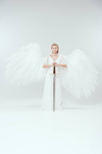 beautiful woman with angel wings holding sword and posing on white background
