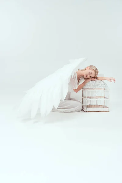 鳥籠に傾いたと白で隔離カメラ目線の翼を持つ天使衣装で美しい女性 — ストック写真