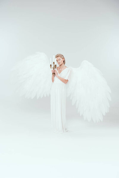 beautiful tender woman in angel costume with wings holding candelabrum with candles isolated on white