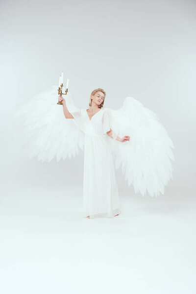 beautiful woman in angel costume with wings holding candelabrum with candles isolated on white