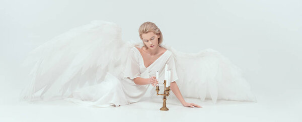 beautiful tender woman in angel costume with wings sitting near candelabrum with candles isolated on white