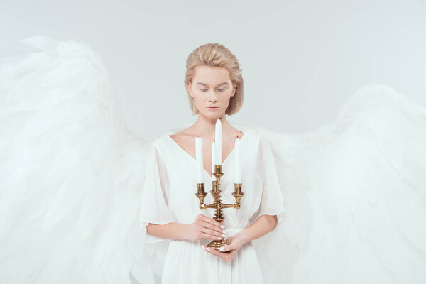 beautiful woman in angel costume with wings with eyes closed holding antique candelabrum isolated on white