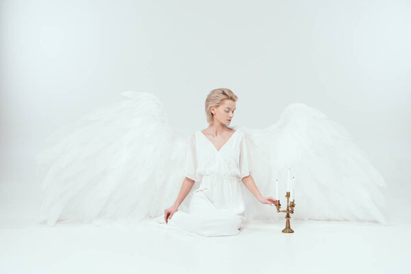 beautiful woman in angel costume with wings sitting near candelabrum with candles isolated on white