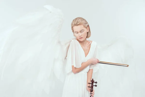 beautiful woman in angel costume with wings and eyes closed holding violin and bow isolated on white