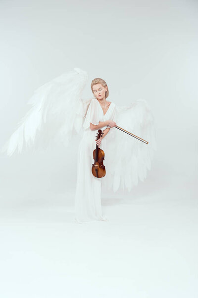 beautiful woman in angel costume with wings holding violin and bow isolated on white
