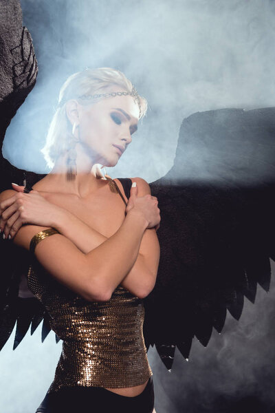 красивая молодая сексуальная женщина с черными крыльями ангела позирует на дымчатом фоне
