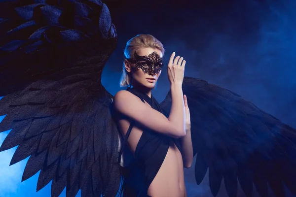 美丽神秘的女人蕾丝面具和黑色天使翅膀看着相机在深蓝色的背景 — 图库照片