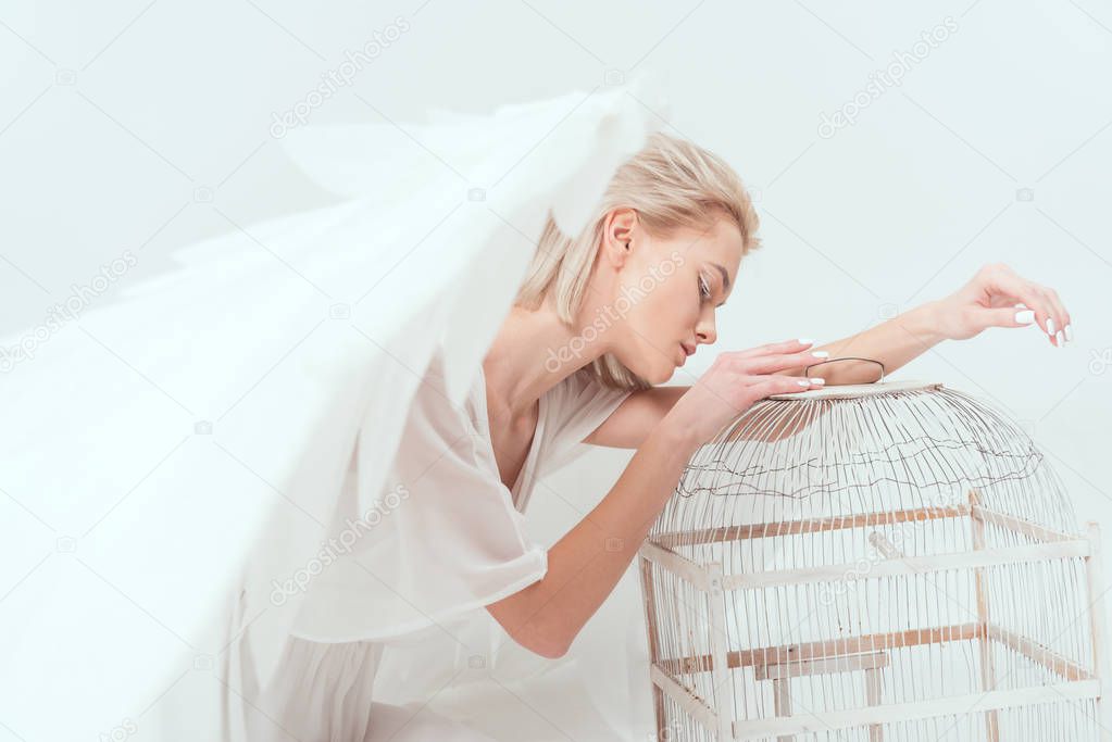 beautiful woman in angel costume with wings leaning on bird cage isolated on white