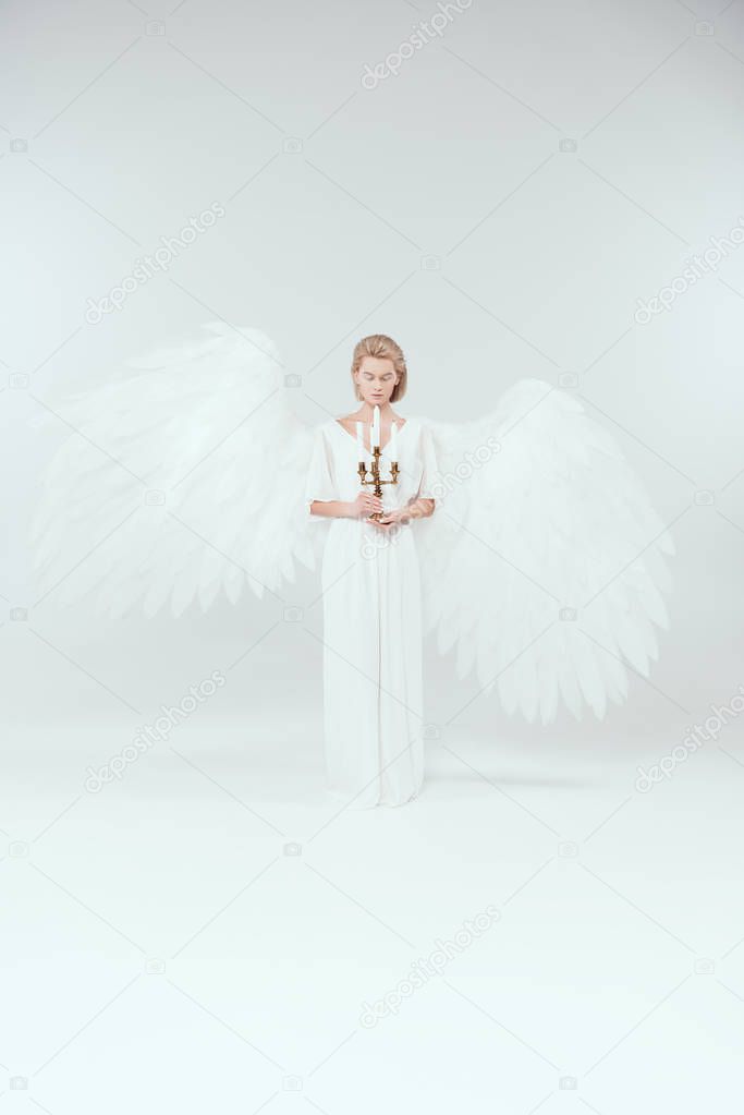 beautiful woman in angel costume with wings and eyes closed holding candelabrum with candles on white background