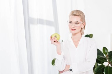 happy businesswoman in glasses holding green apple in office  clipart