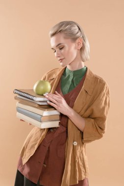 Eko giyim üzerinde bej izole kitap ve duran yeşil elma tutan güzel kız