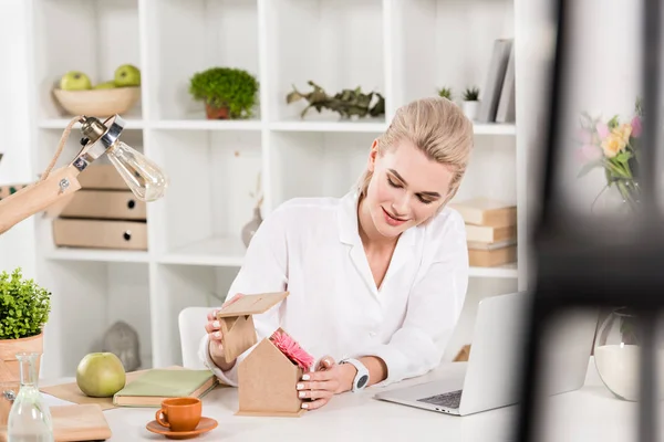 Cheerful Woman Looking Pink Flower Small Cardboard House Laptop Office — Stock Photo, Image