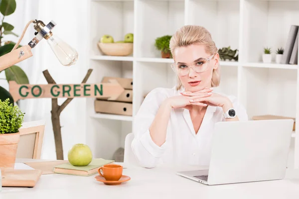 Attraktive Frau Brille Sitzt Neben Laptop Mit Grünem Schild Dahinter — Stockfoto