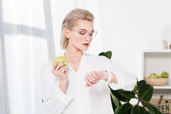 Hermosa Mujer Negocios Gafas Mirando Reloj Mientras Sostiene Manzana Verde —  Fotos de Stock