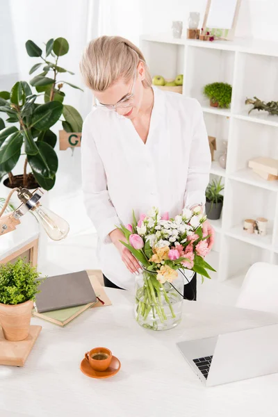 Mujer Alegre Mirando Flores Jarrón Cerca Computadora Portátil Taza Oficina — Foto de Stock