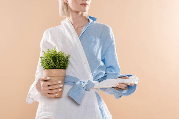 cropped view of woman holding pot with plant and standing in eco clothing isolated on beige, environmental saving concept 