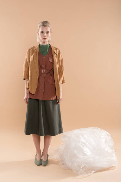 blonde girl wearing eco clothing standing near polyethylene on beige background, environmental saving concept