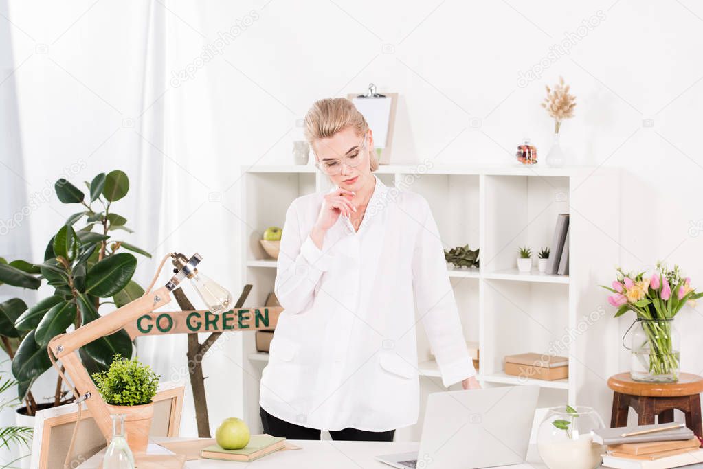 attractive woman in glasses standing near laptop with go green sign behind, environmental saving concept 