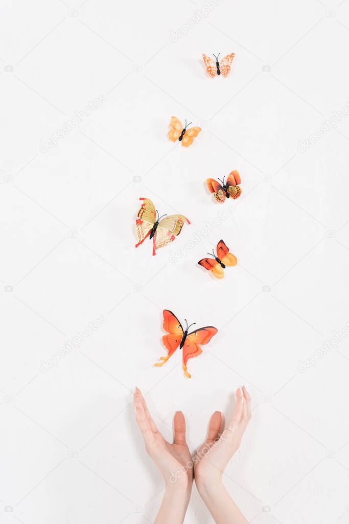cropped view of female hands near orange butterflies flying on white background, environmental saving concept 