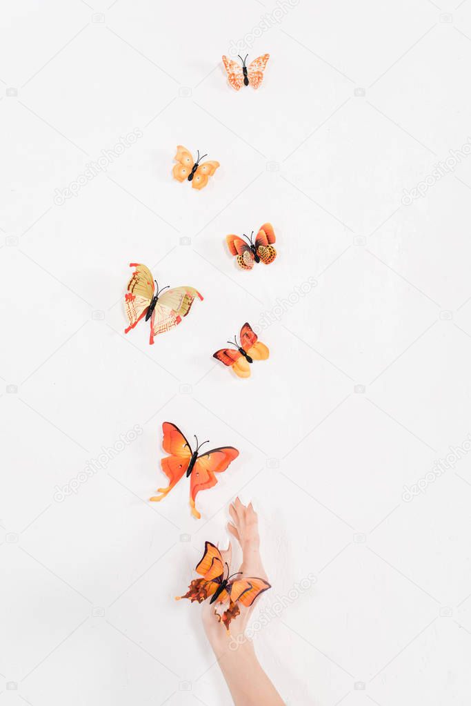 cropped view of hand near orange butterflies flying on white background, environmental saving concept 