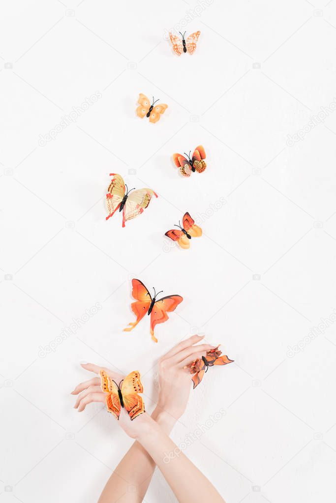 cropped view of woman with crossed arms near orange butterflies flying on white background, environmental saving concept 