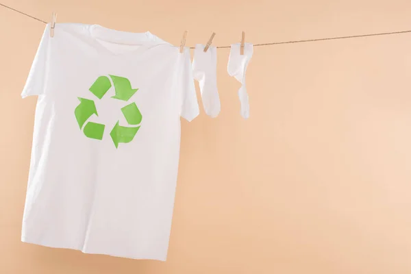 t-shirt with recycling sign on clothesline near white socks isolated on beige, environmental saving concept