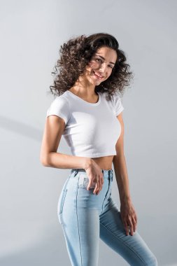 Gri arka plan üzerinde gülümseme ile poz Jeans düzgün kıvırcık kız