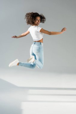 Gri arka plan üzerinde atlama Jeans kıvırcık kadın gülüyor