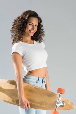 Gri izole longboard tutan düzgün kıvırcık kız