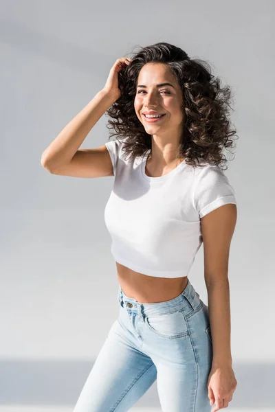 Cheerful Young Woman Jeans Touching Curly Hair Grey Background — Stock Photo, Image