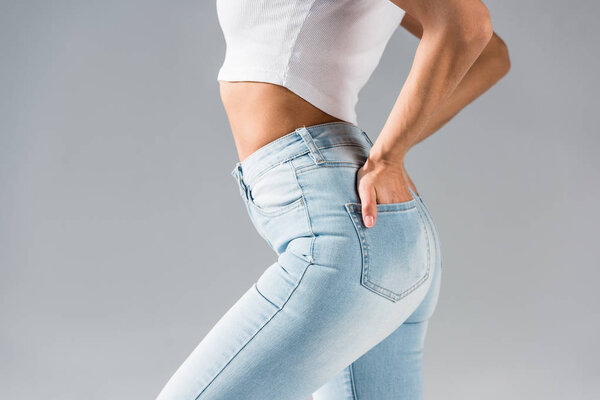Cropped shot of sexy girl in jeans with hands in pockets isolated on grey