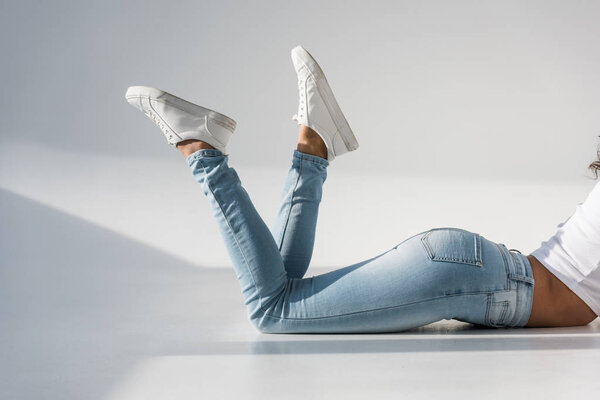 Обрезанный вид девушки в джинсах лежащих на сером фоне
