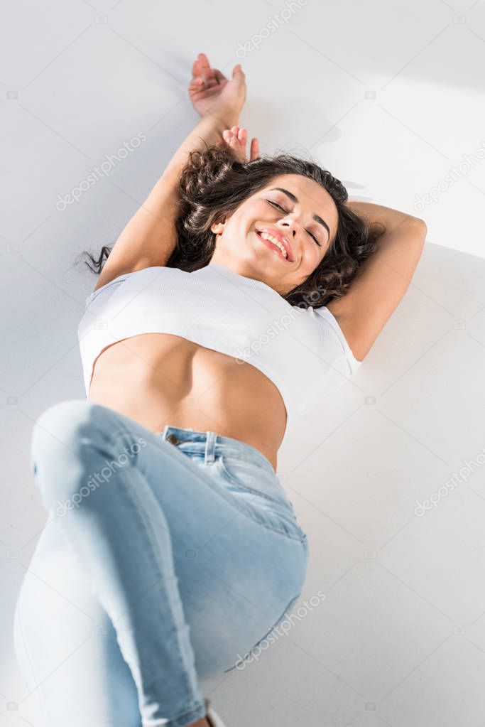 Sexy smiling girl in jeans lying on light surface