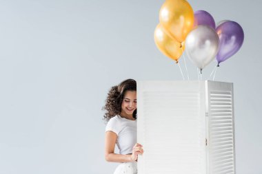 Gri arka plan üzerinde gülümseyen hava balonları ile mutlu kıvırcık kız